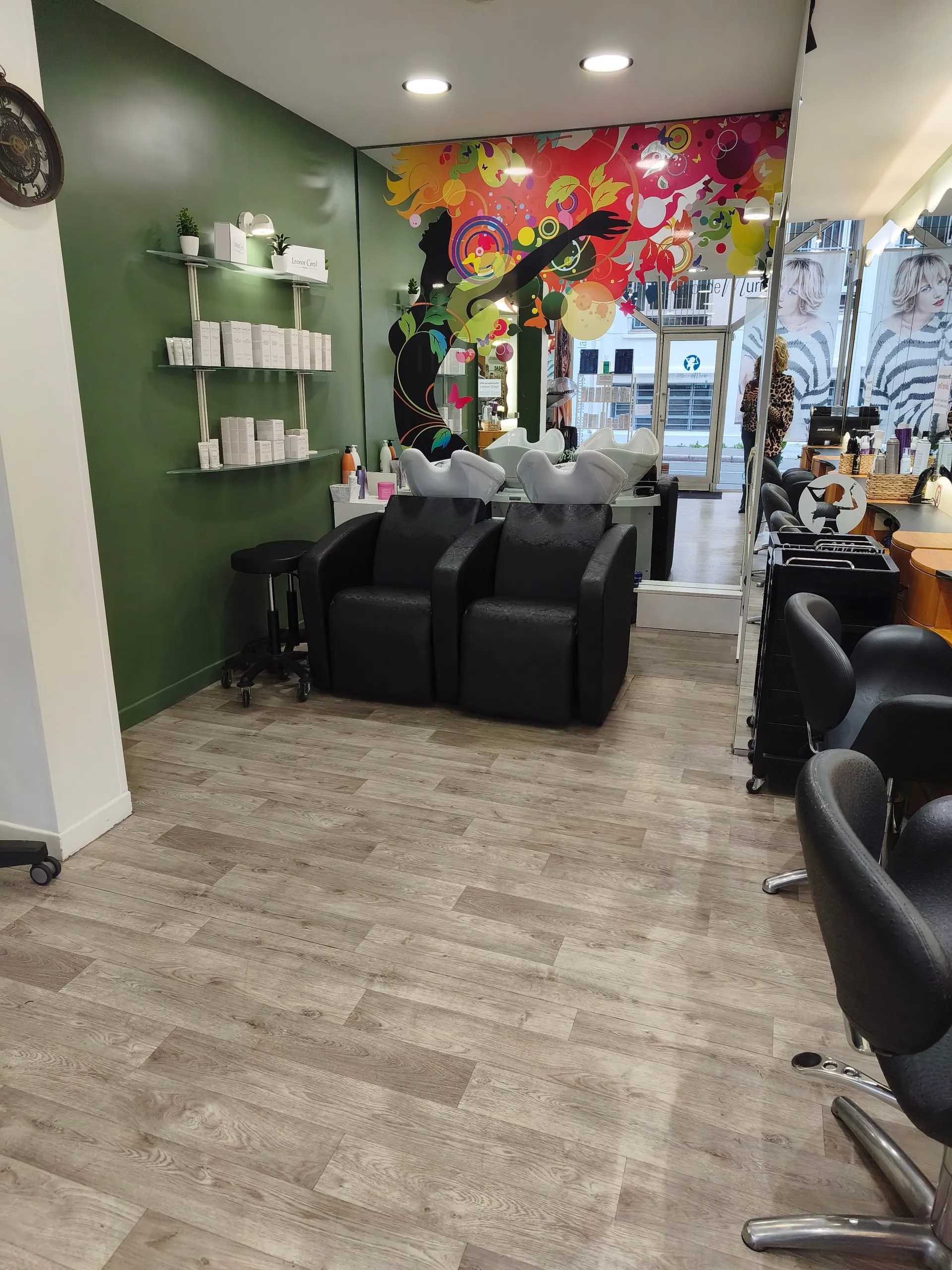 Bacs à shampoing et fauteuils noirs devant une fresque colorée, mur vert et étagères de produits